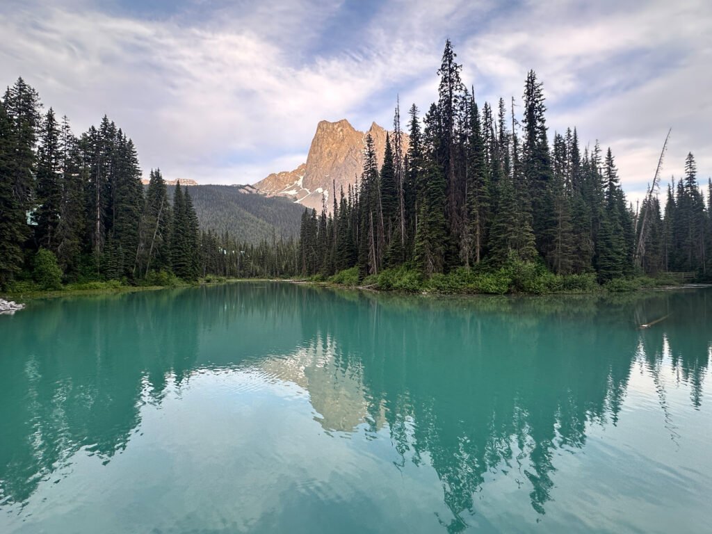 Calm alpine water reflects surrounding forest and distant peaks.